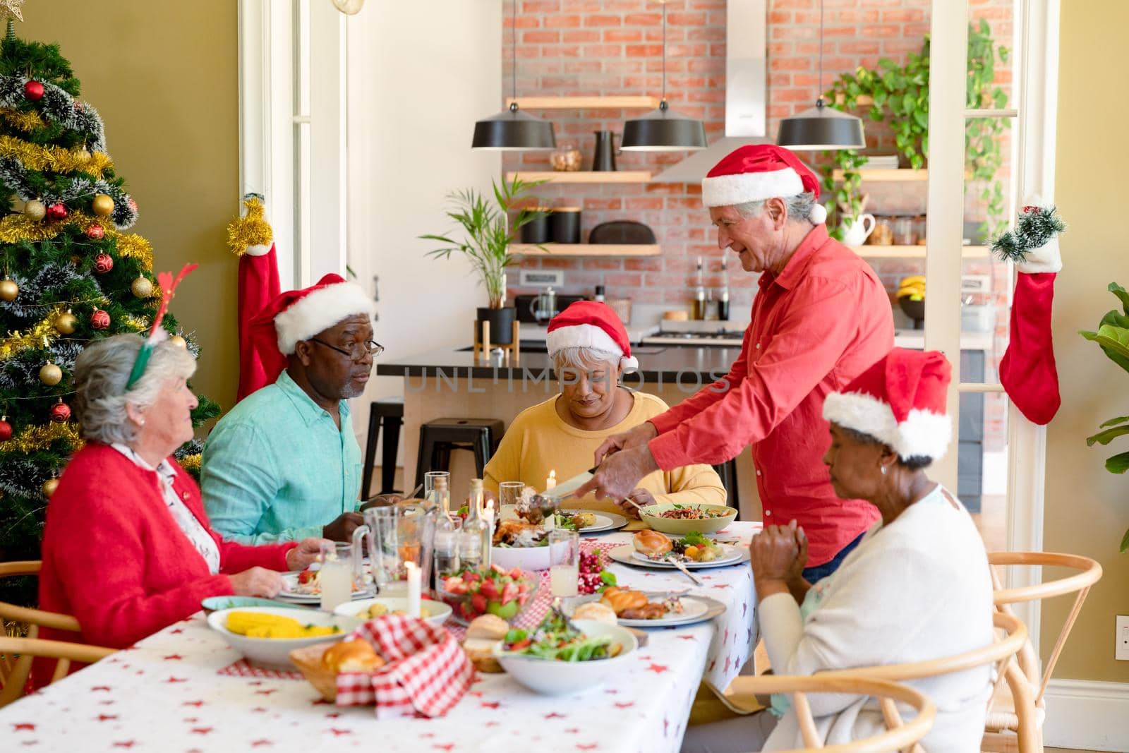 Diverse group of happy senior friends in holiday hats celebrating christmas together at home. christmas festivities, celebrating at home with friends.