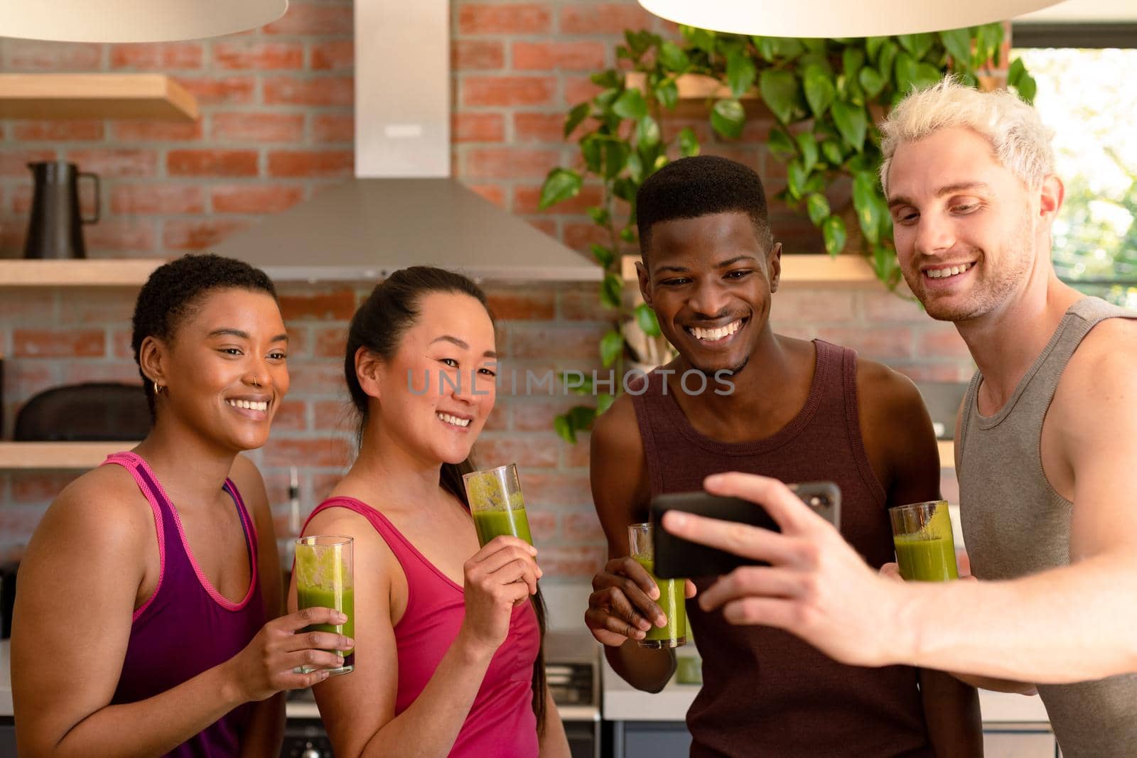 Group of diverse female and male friends preparing smoothie together and taking selfie by Wavebreakmedia