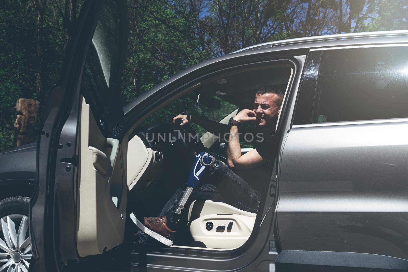 a man on a prosthetic leg sits in a car. Dressed in black jeans and a T-shirt. travel concept, freedom of movement