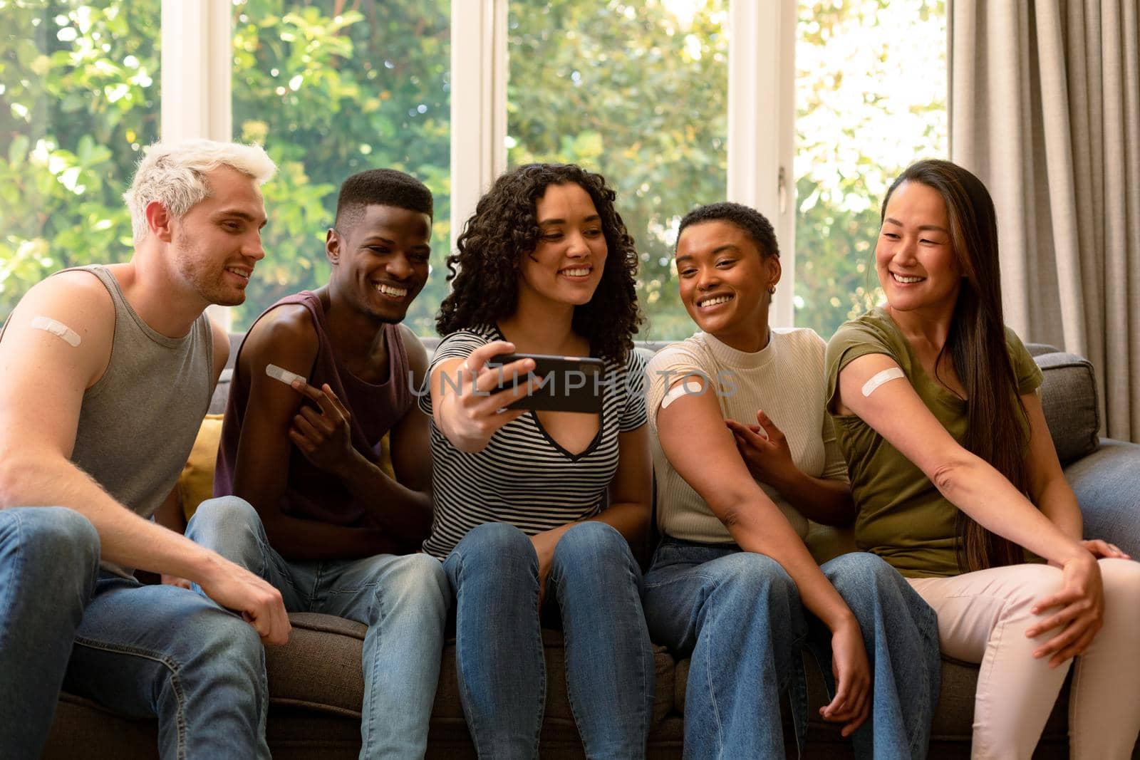 Group of happy diverse female and male friends showing plasters after vaccination and taking selfie by Wavebreakmedia