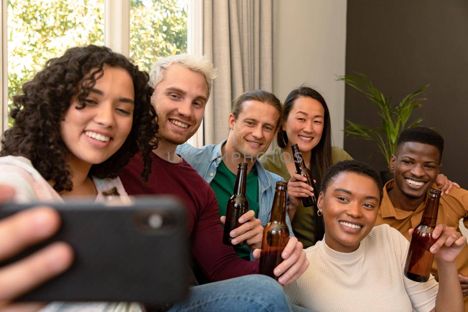 Group of happy diverse female and male friends drinking beer together and taking selfie by Wavebreakmedia