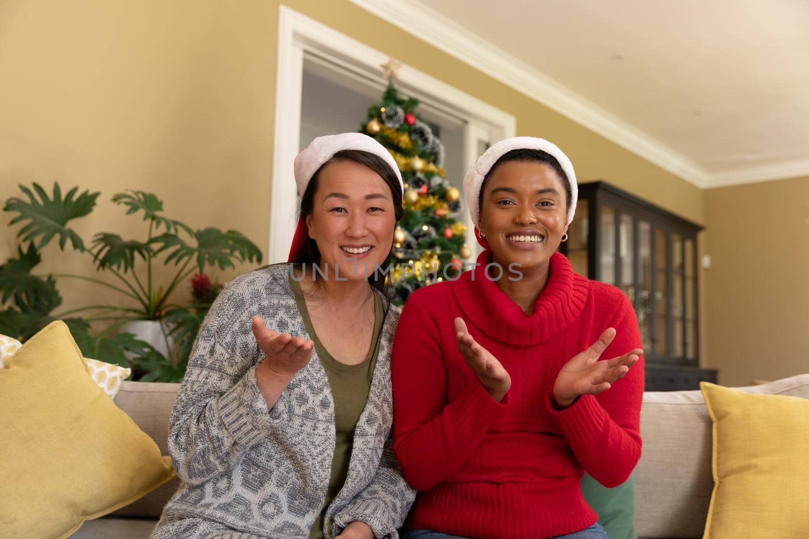 Two happy diverse female friends in santa hats having video call at christmas time. christmas, festivity and communication technology.