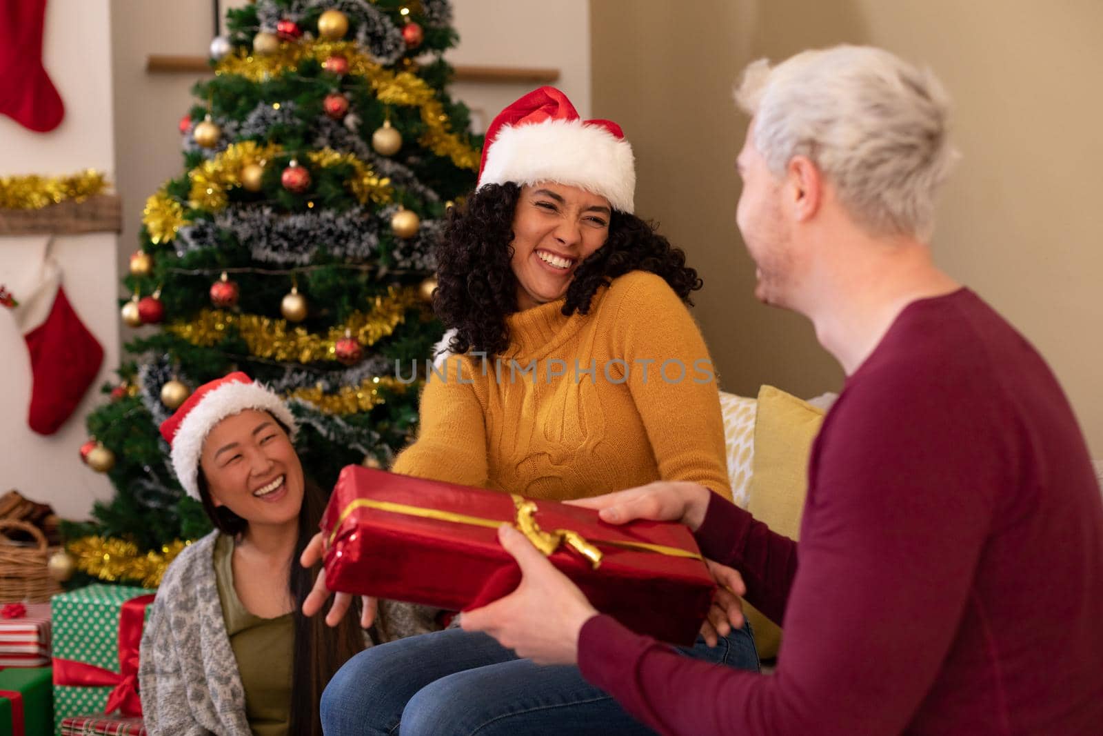 Happy diverse female and male friends sharing presents at christmas time. christmas festivities, celebrating at home with friends.