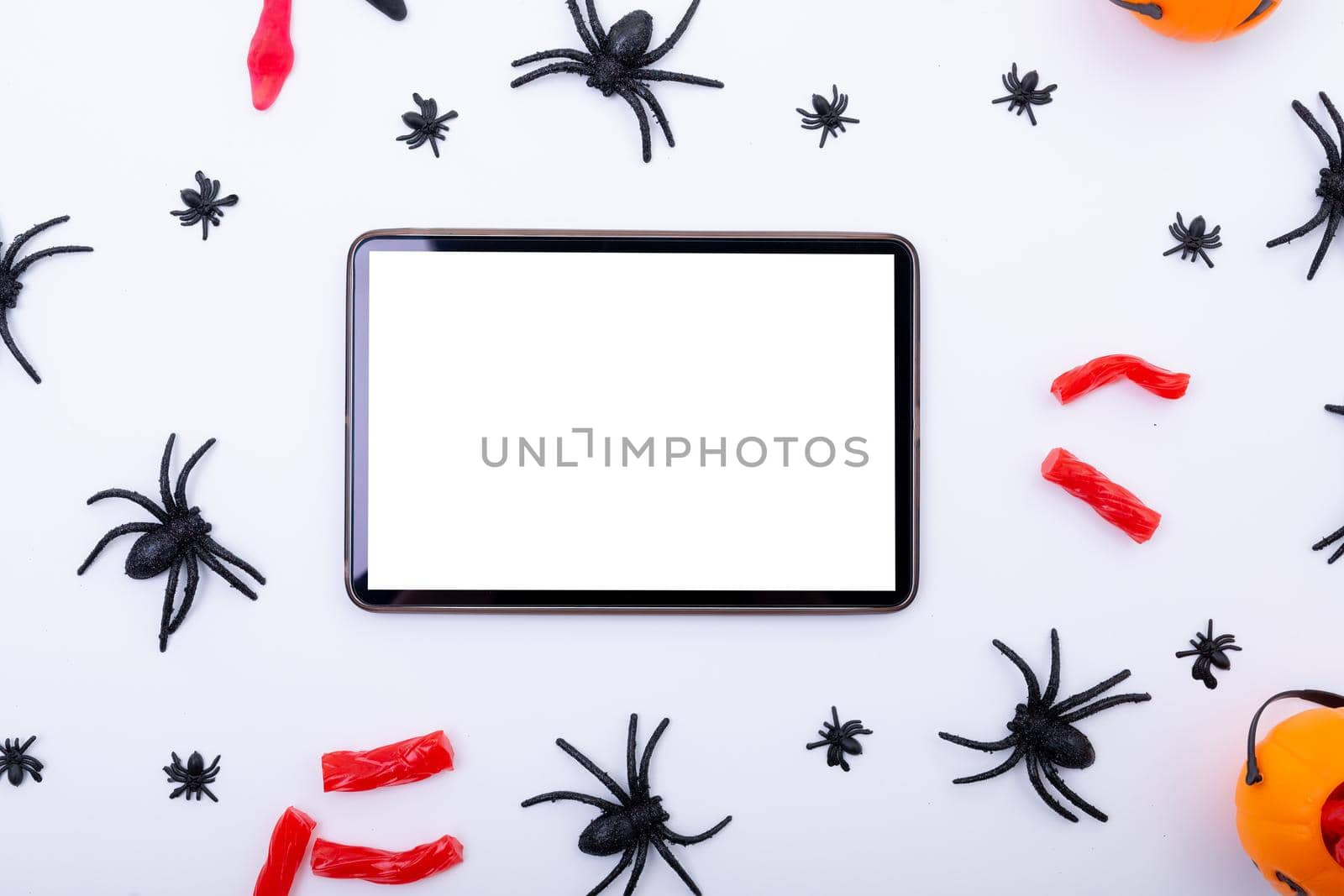 Composition of halloween spiders and sweets and tablet with copy space on white background. halloween tradition and celebration concept.