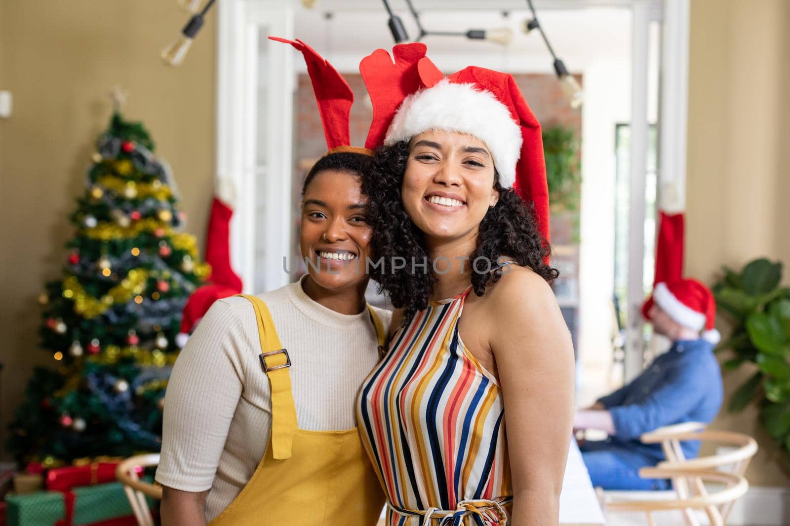 Two diverse female friends in santa hats embracing, taking photo, celebrating christmas at home by Wavebreakmedia