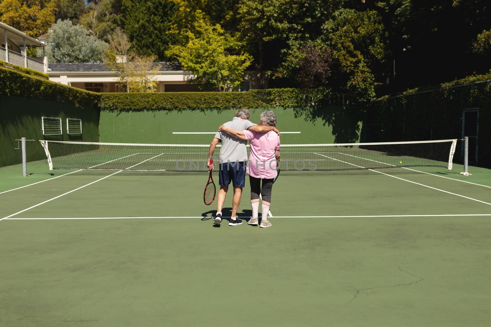 Senior caucasian couple embracing and walking on tennis court. retirement retreat and active senior lifestyle concept.