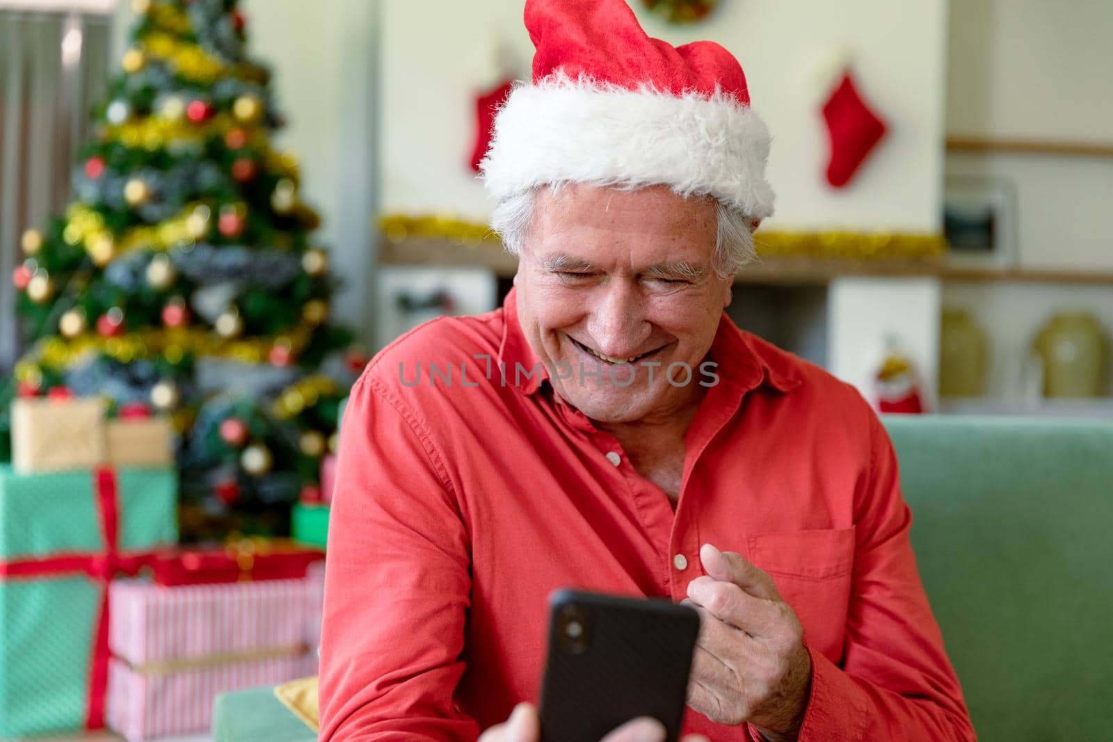 Happy caucasian senior man wearing santa hat having video call on smartphone at christmas time. christmas, festivity and communication technology.