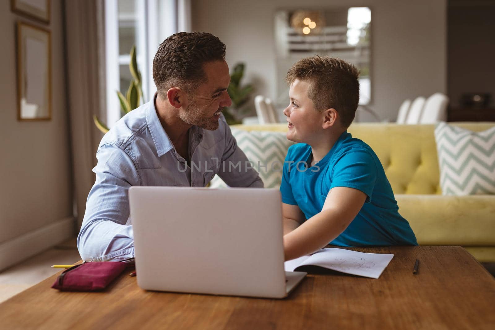 Caucasian father using laptop to help his son with homework at home. home schooling and education concept