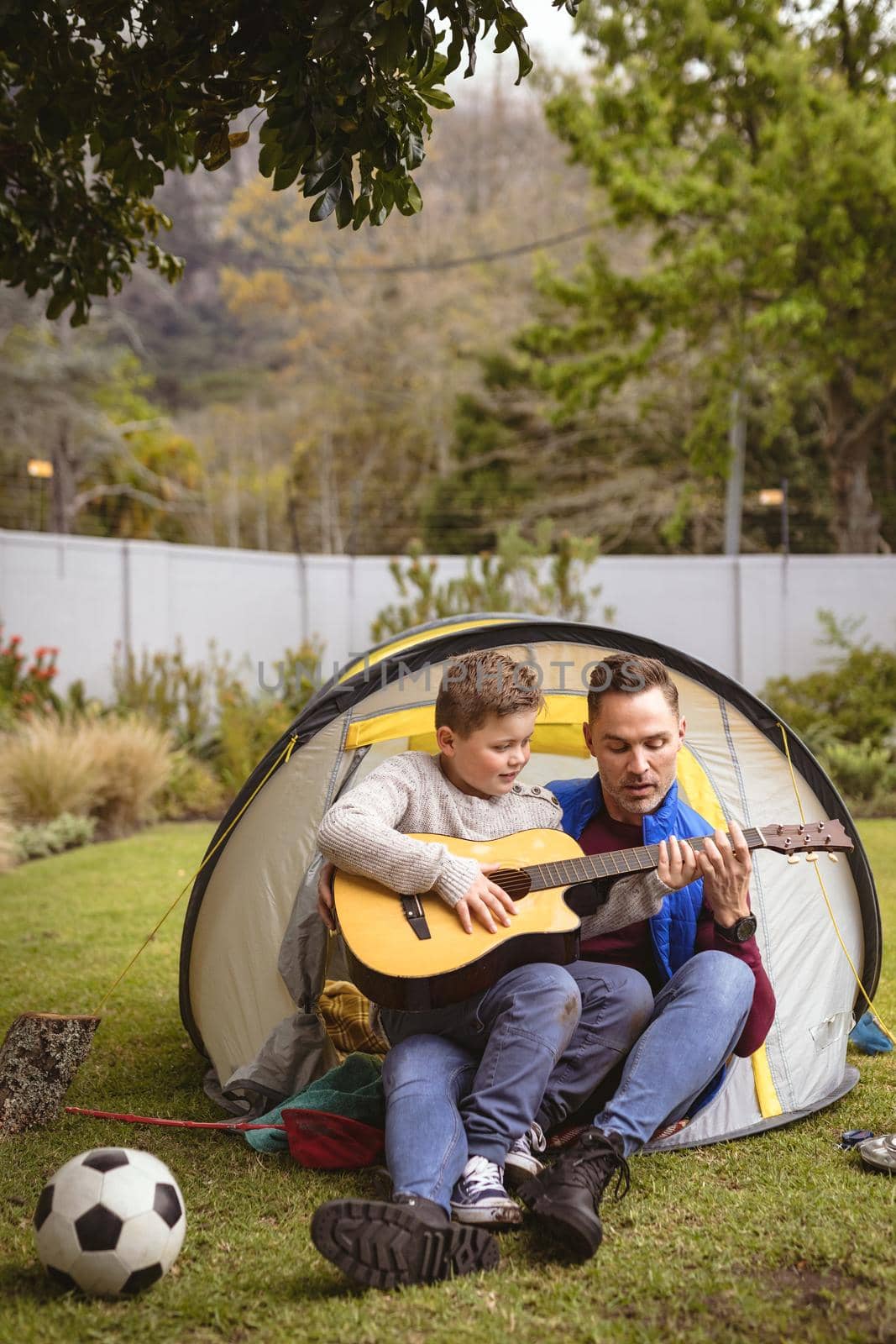 Caucasian father and son playing guitar together while sitting in a tent in the garden by Wavebreakmedia