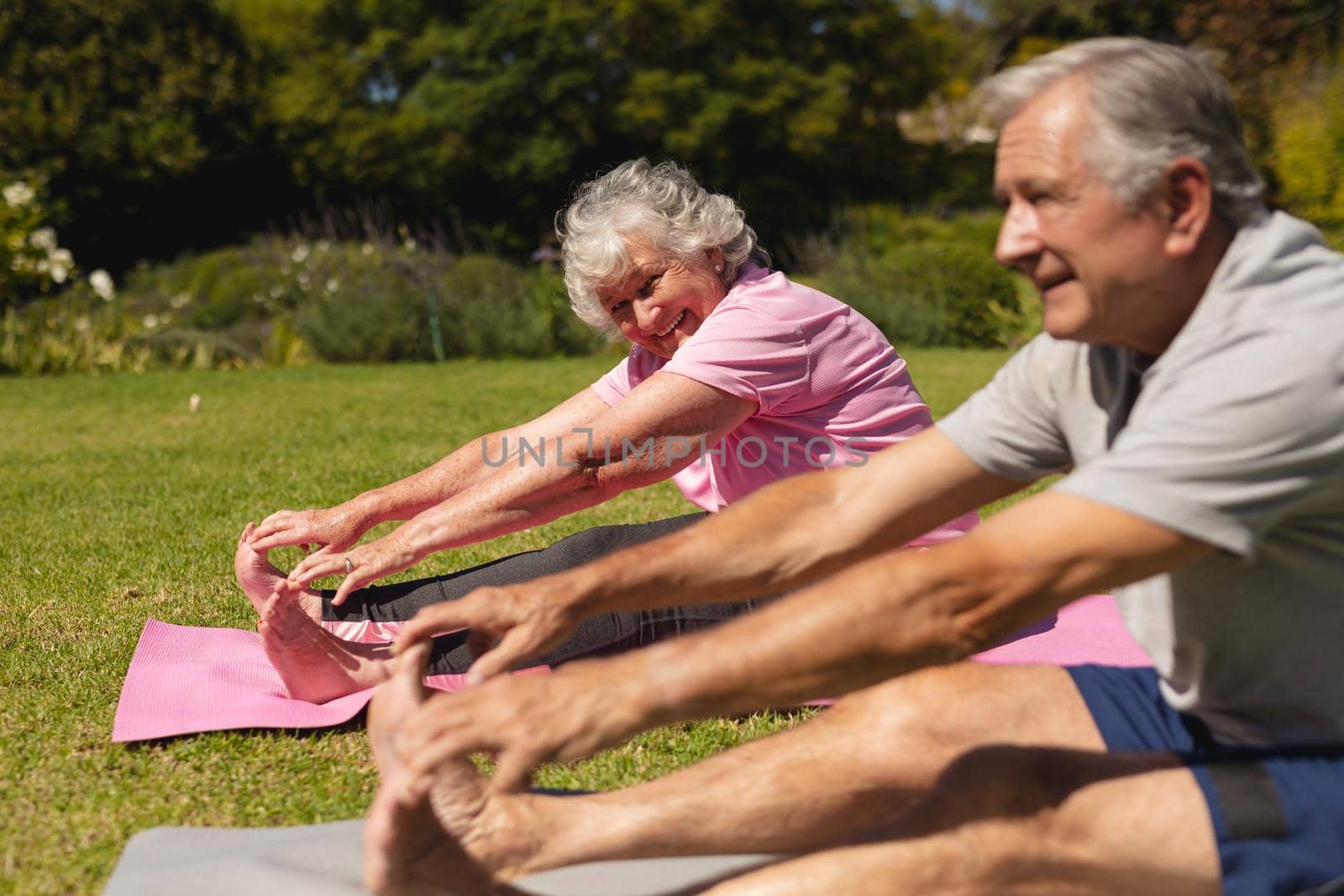 Senior caucasian couple practicing yoga, stretching in sunny garden by Wavebreakmedia
