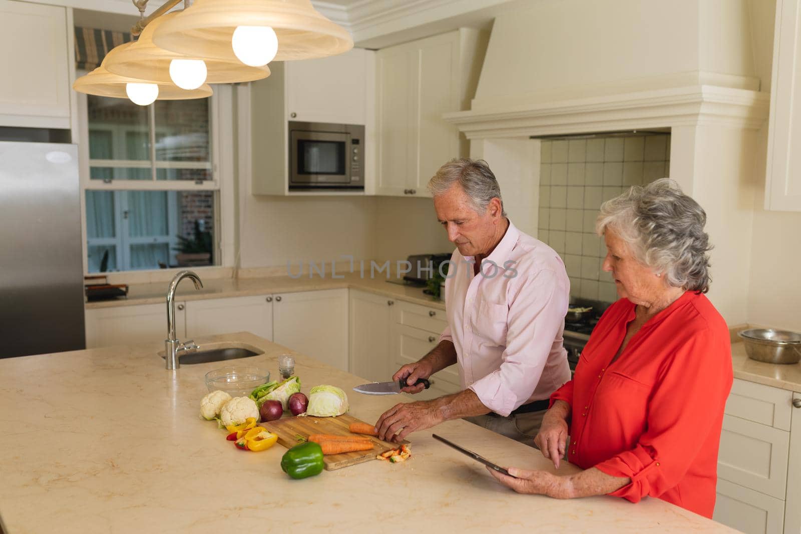 Senior caucasian couple cooking together and using tablet in kitchen. retreat, retirement and happy senior lifestyle concept.