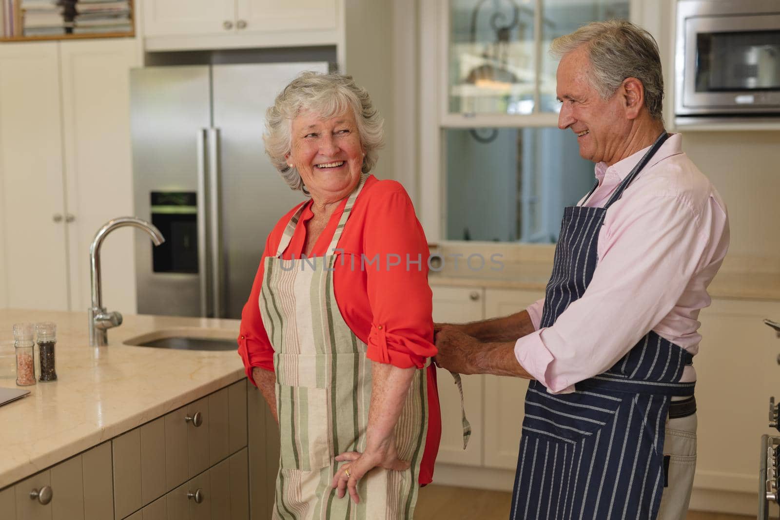 Senior caucasian couple tying apron and smiling in kitchen by Wavebreakmedia