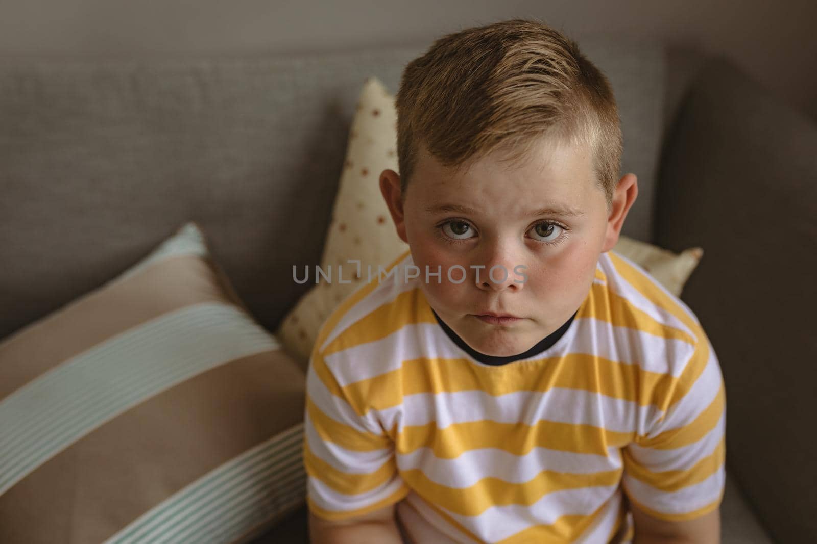 Portrait of caucasian boy looking up while sitting on the couch at home. childhood and home concept