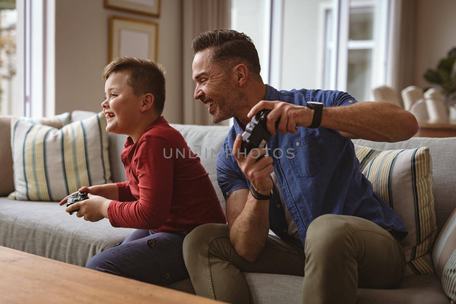 Caucasian father and son playing video games together sitting on the couch at home. fatherhood and love concept
