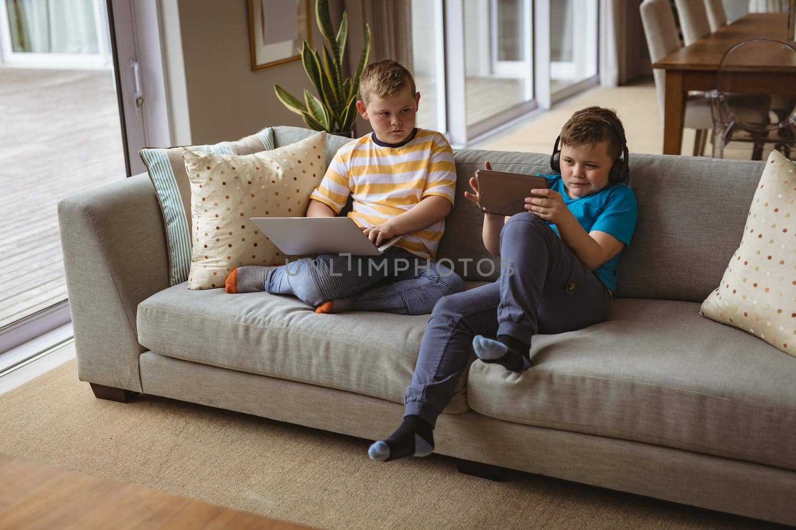 Two caucasian boys using laptop and digital tablet sitting on the couch at home by Wavebreakmedia