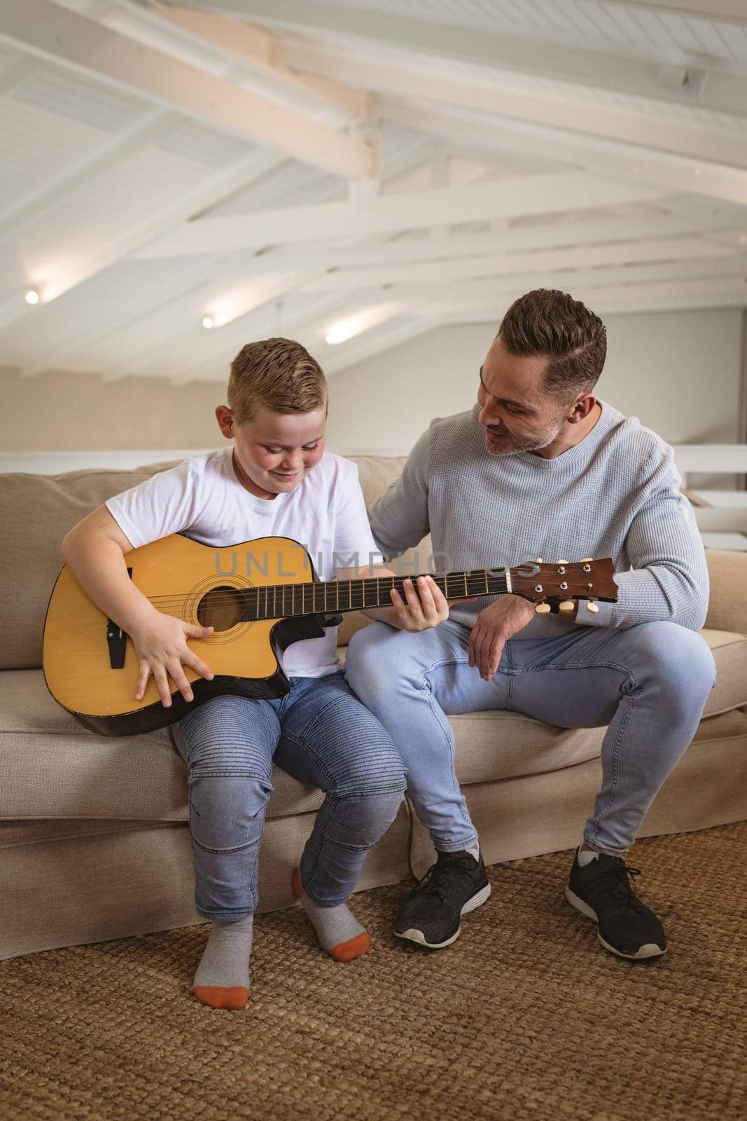 Caucasian father teaching his son to play guitar sitting on the couch at home. childhood and hobby concept