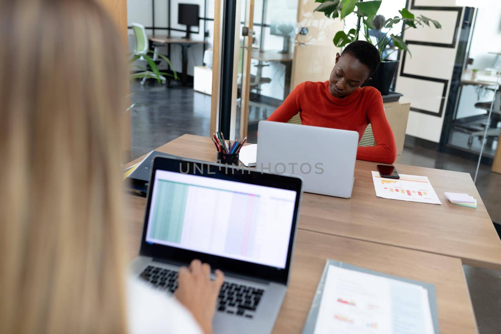 Diverse female business colleagues sitting at desks using laptop making notes. business in a modern office.