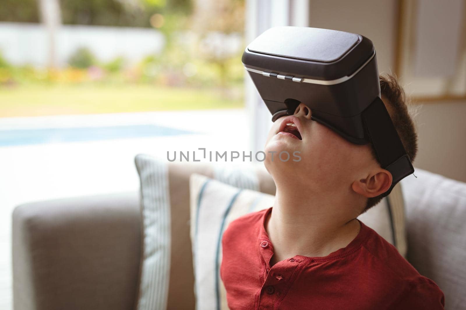Caucasian boy wearing vr headset looking up sitting on the couch at home. gaming and entertainment concept