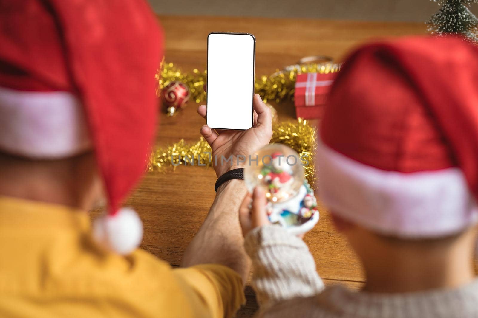 Rear view of father and son having a video call on smartphone with copy space during christmas. social distancing during covid 19 pandemic at christmas time