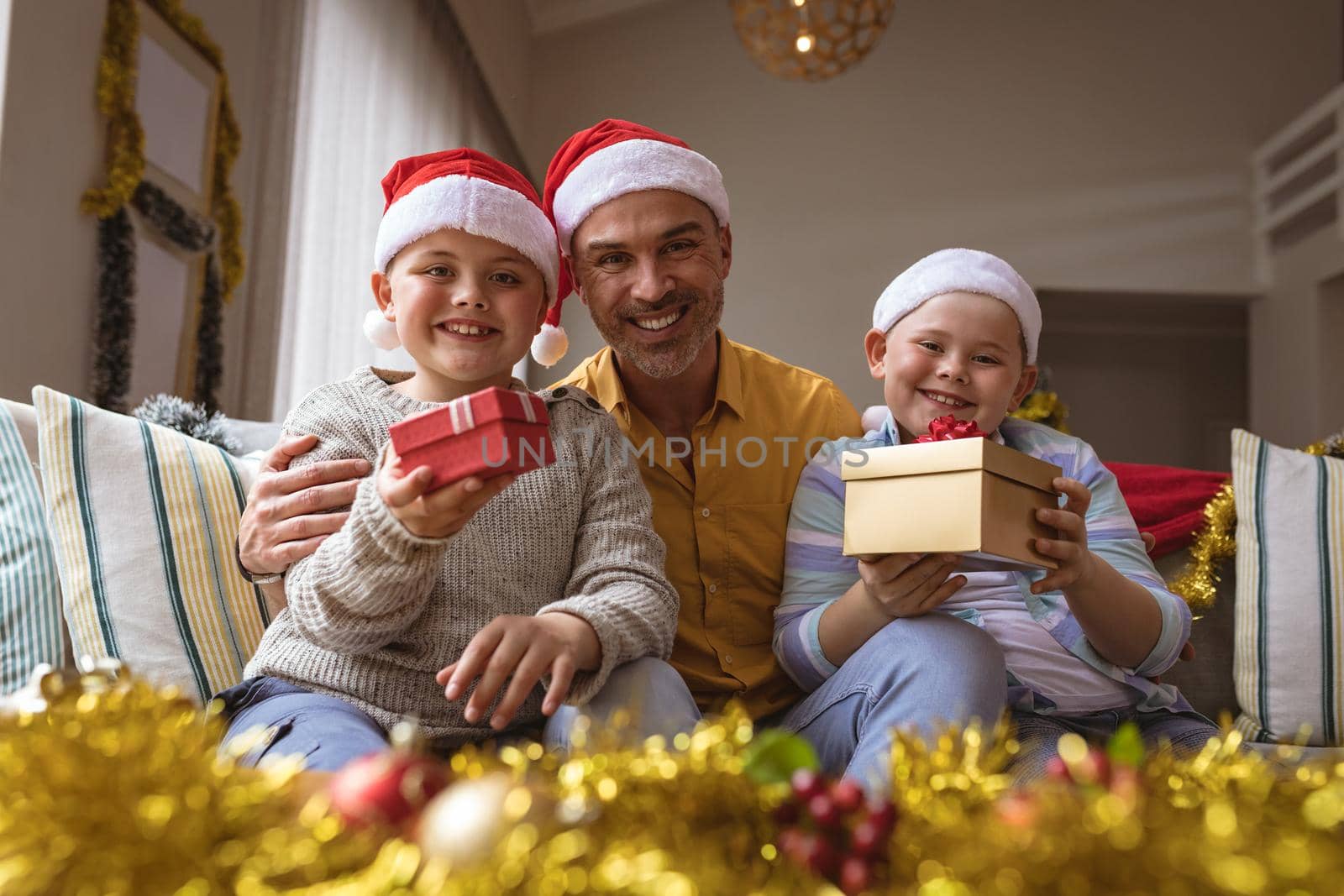 Portrait of caucasian father and two sons holding christmas gifts smiling at home during christmas. christmas festivity and celebration concept