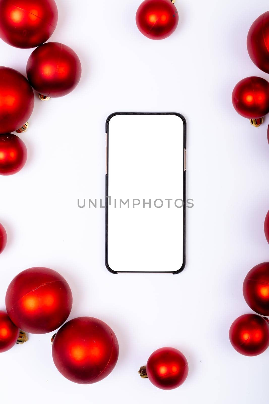 Composition of smartphone with copy space and red baubles on white background. christmas, tradition and celebration concept.