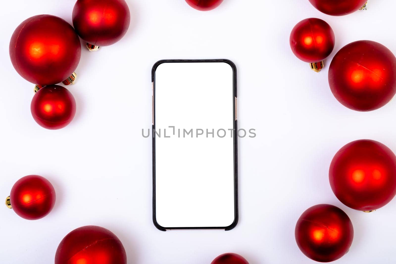 Composition of smartphone with copy space and red baubles on white background. christmas, tradition and celebration concept.