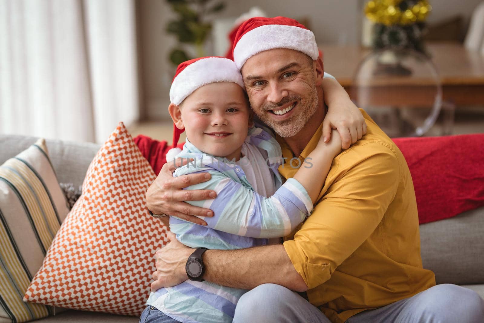 Portrait of caucasian father and son hugging and smiling at home during christmas. christmas festivity and celebration concept