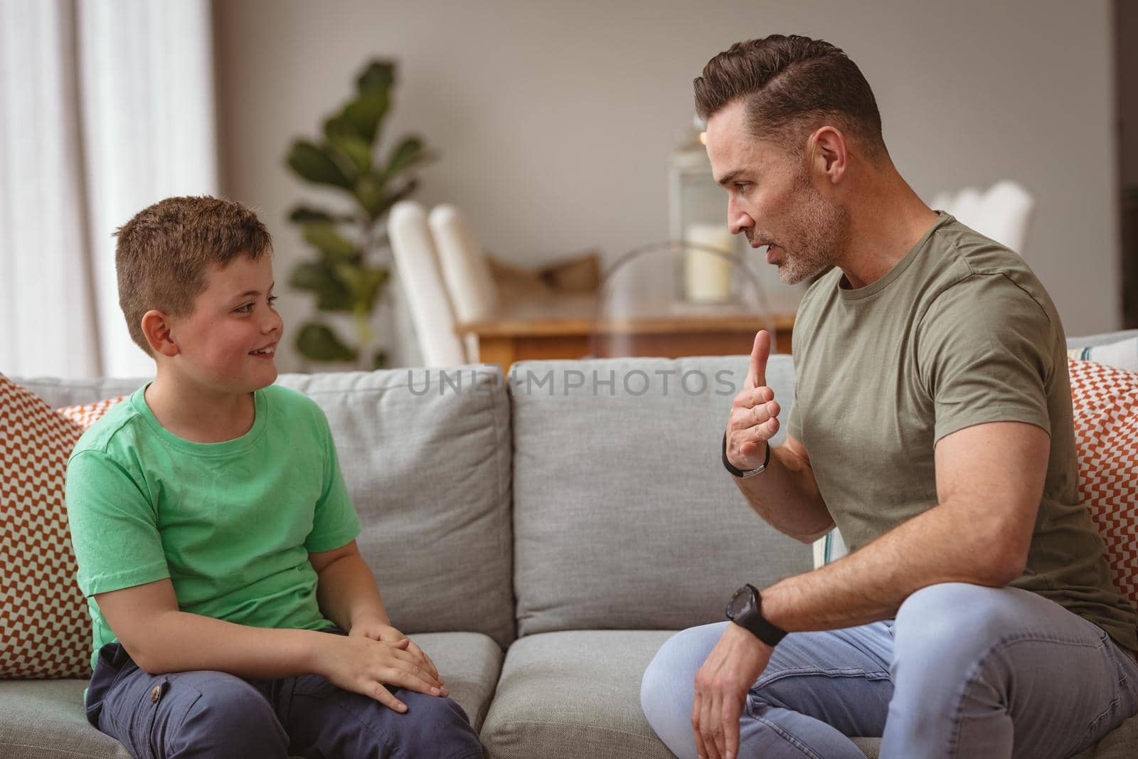 Caucasian father and son communicating using sign language while sitting on the couch at home by Wavebreakmedia