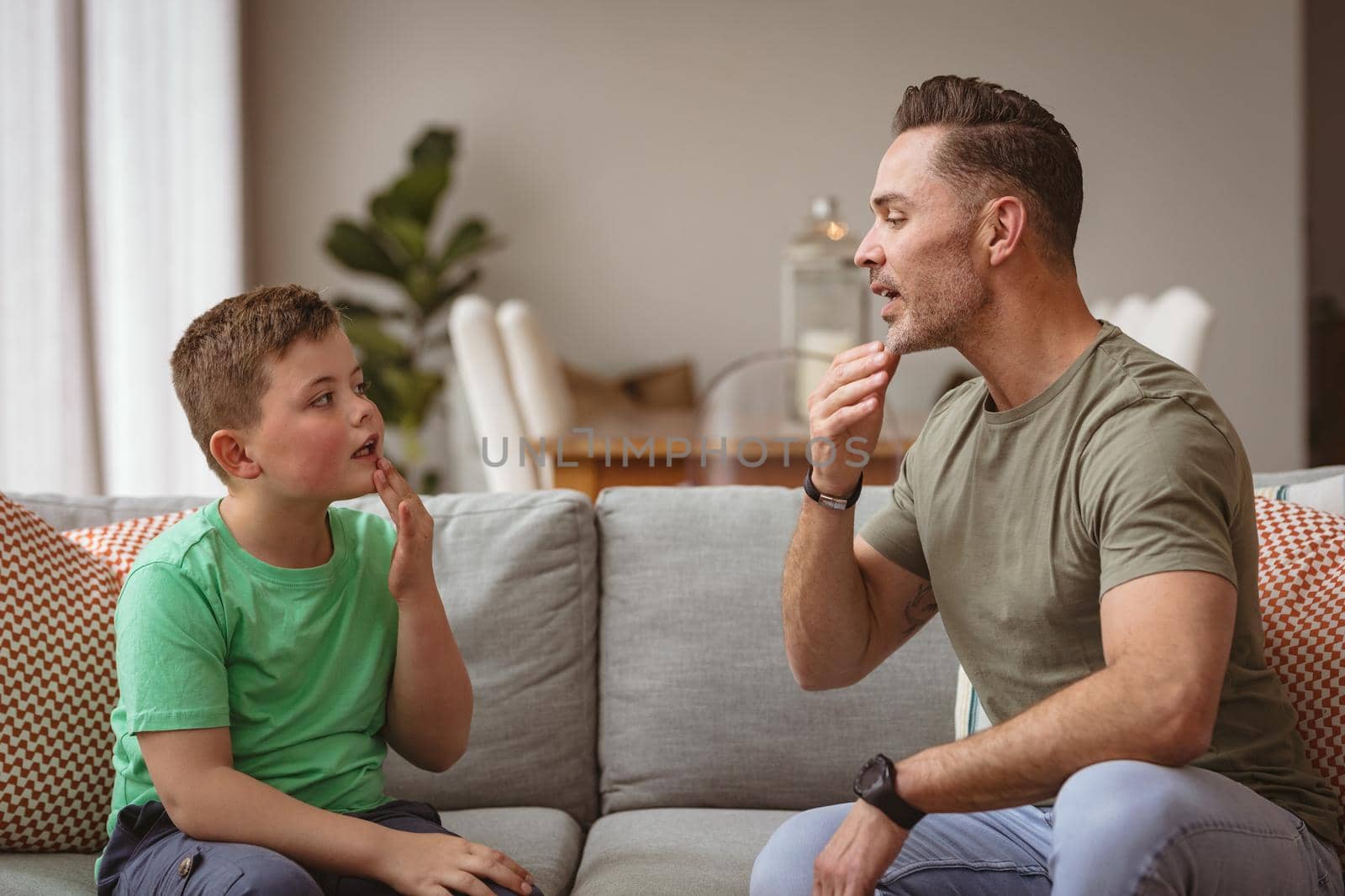 Caucasian father and son communicating using sign language while sitting on the couch at home. sign language learning concept