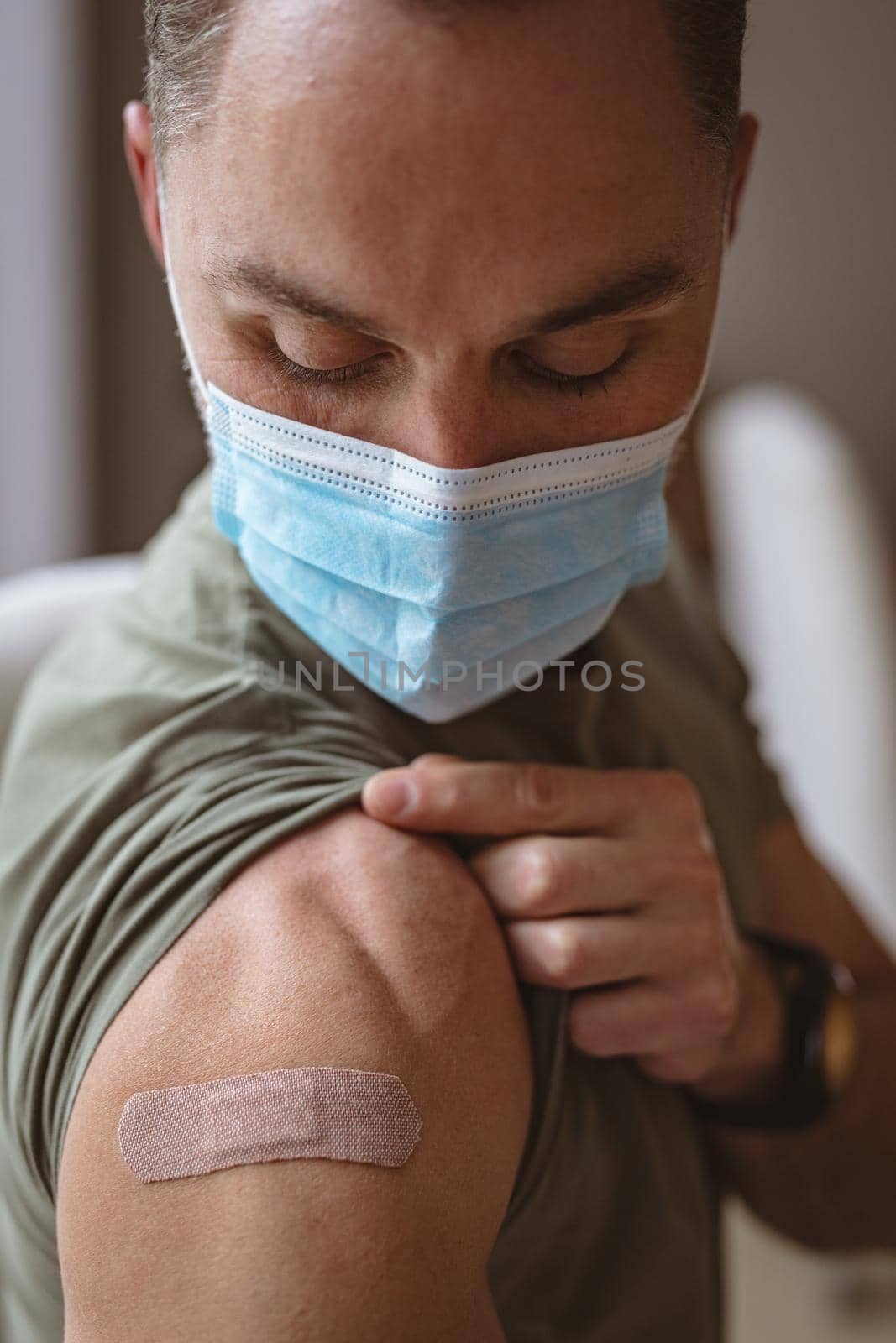 Caucasian man wearing face mask showing his vaccinated shoulder at home. vaccination for prevention of coronavirus outbreak concept