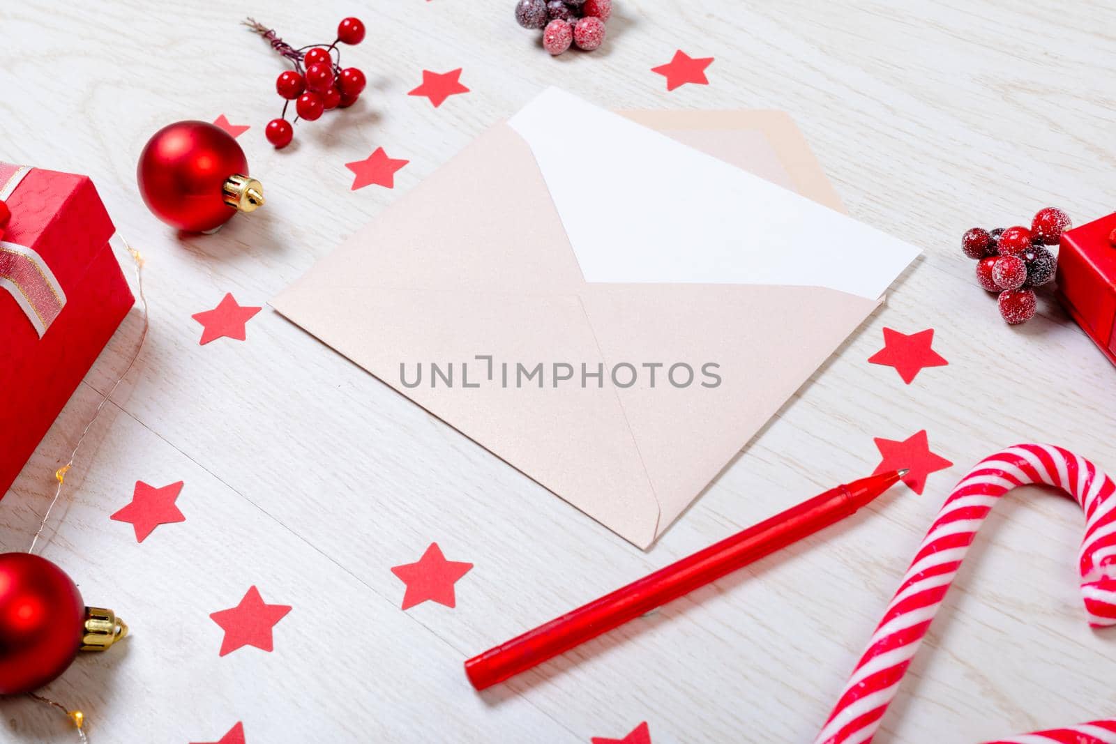 Composition of christmas decorations with envelope and red stars on white wooden background by Wavebreakmedia