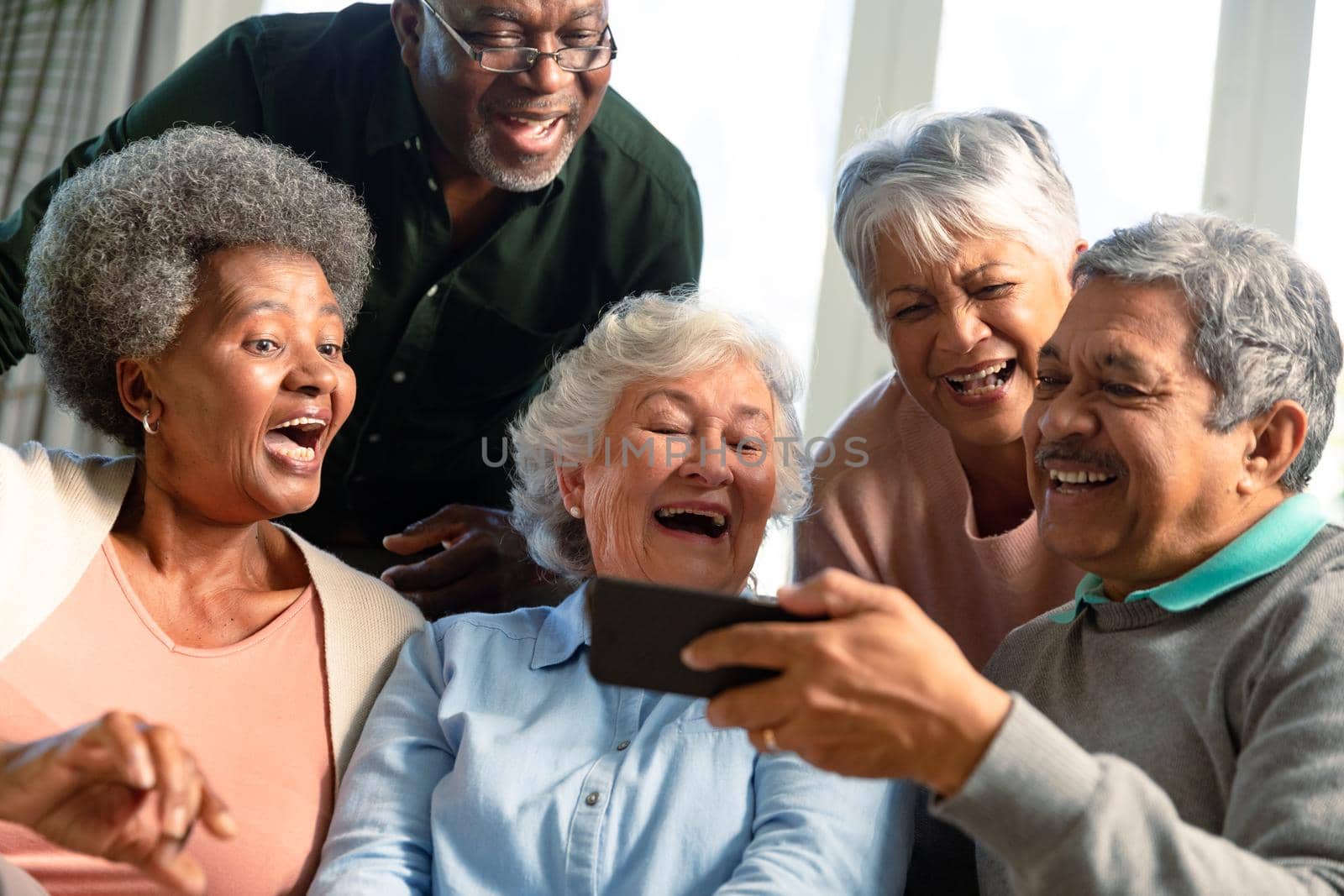 Five happy diverse senior friends sitting on sofa and looking at smartphone by Wavebreakmedia