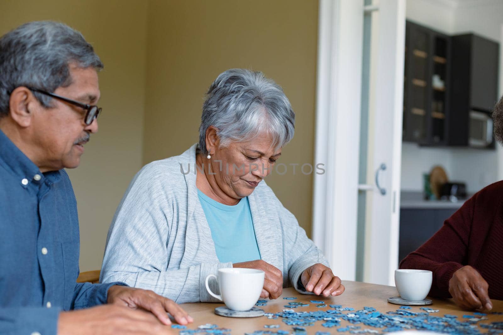 Two diverse female and male friends sitting at table and doing puzzles by Wavebreakmedia