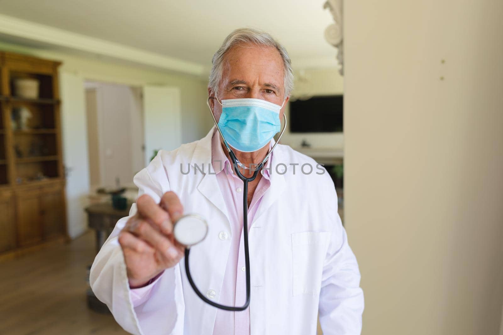 Portrait of senior caucasian male doctor wearing face mask holding stethoscope looking at camera by Wavebreakmedia