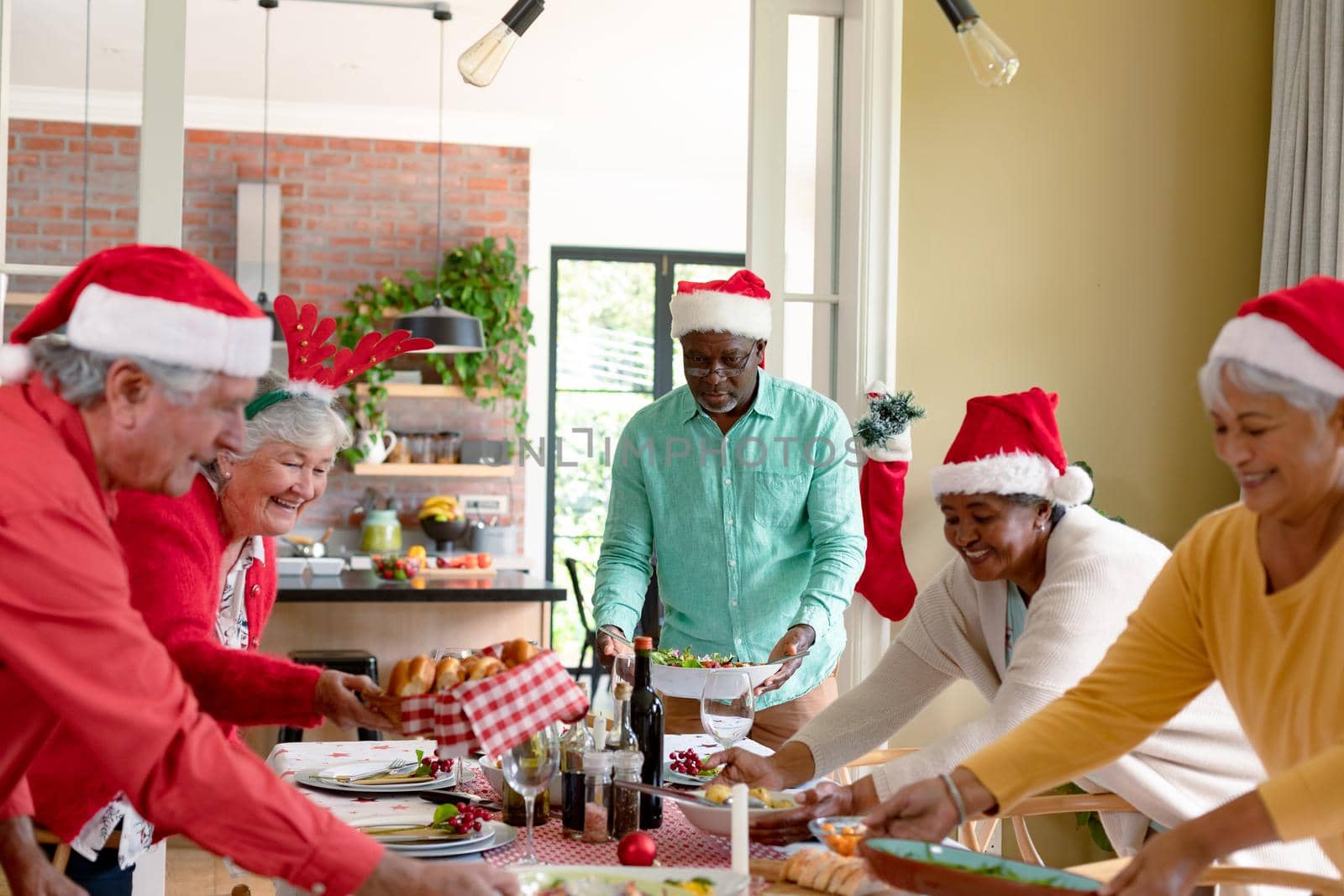 Diverse group of happy senior friends in holiday hats celebrating christmas together at home. christmas festivities, celebrating at home with friends.