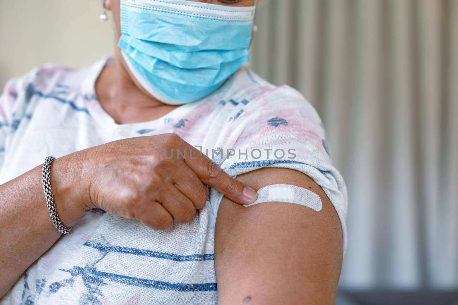 Senior mixed race woman in face mask showing plaster after vaccination. senior health and lifestyle during covid 19 pandemic.