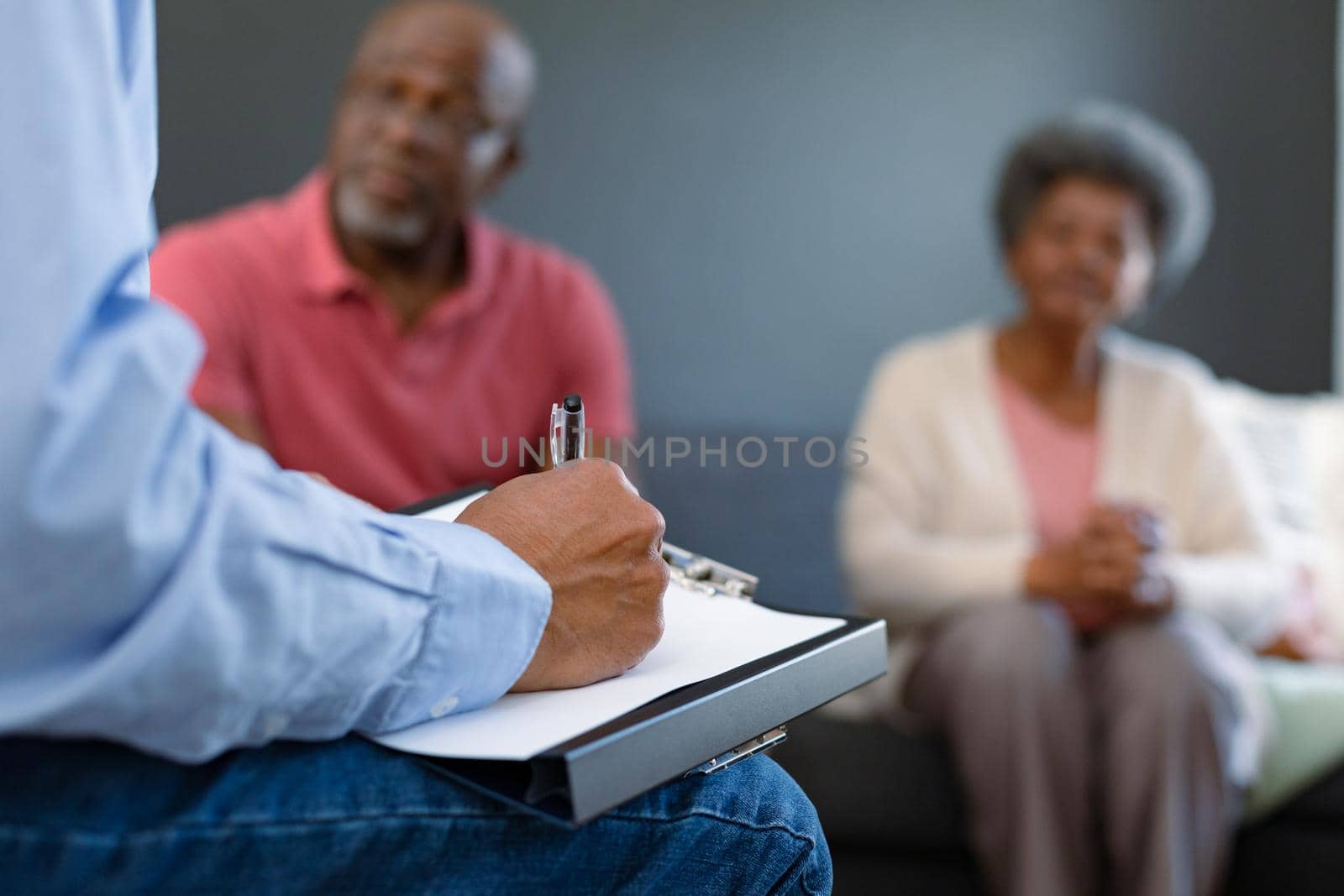 Hand of mixed race senior male counsellor iwth clipboard advising diverse group of senior friends by Wavebreakmedia