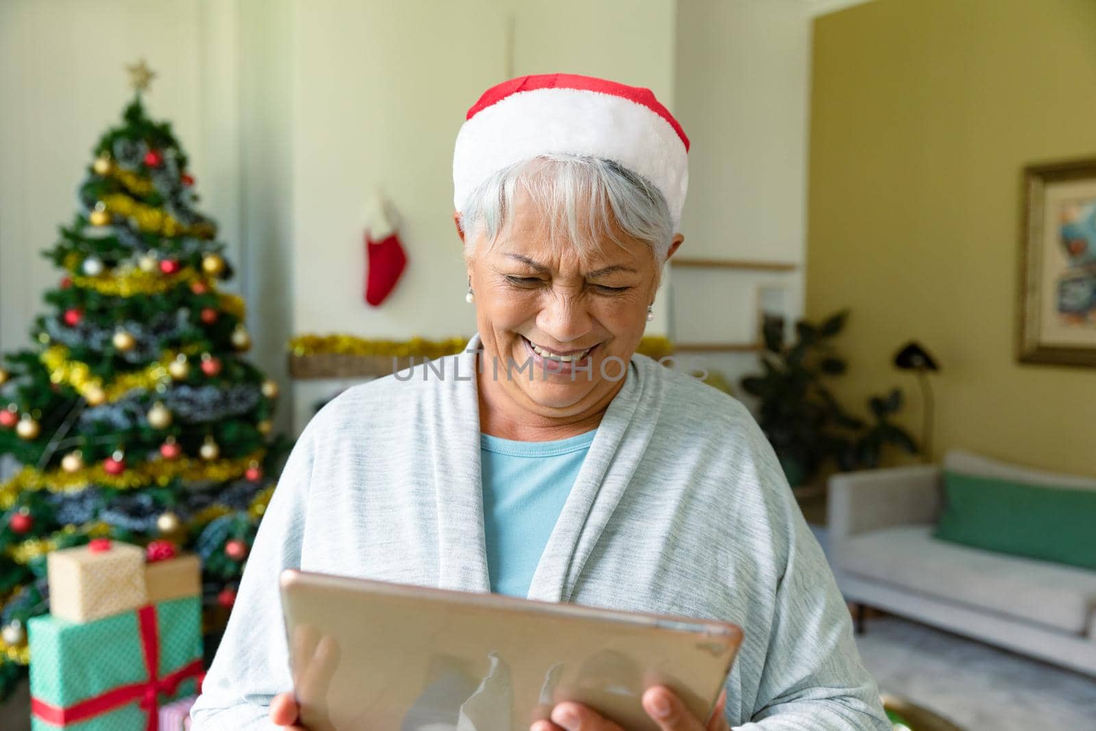 Happy mixed race senior woman in santa hat using tablet at christmas time. christmas, festivity and communication