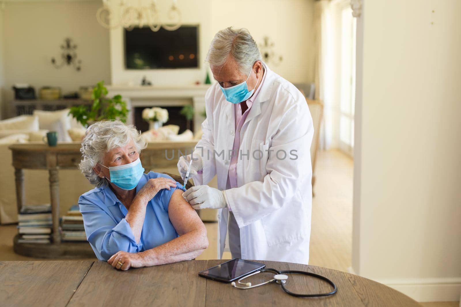 Senior caucasian male doctor vaccinating female patient wearing face masks. medicine and healthcare services during covid 19 pandemic concept.