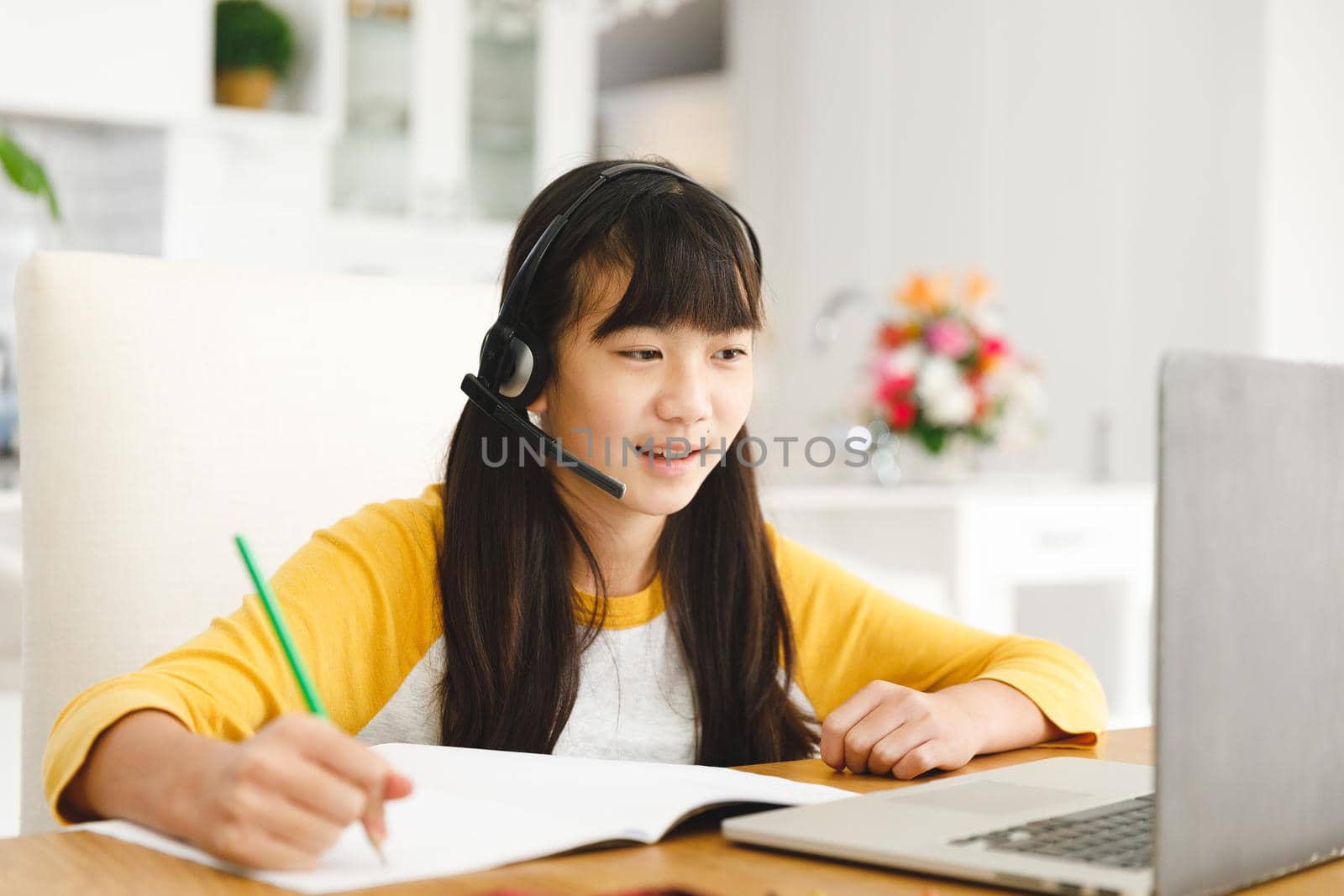 Asian girl sitting at table and using laptop during online lessons. childhood, education and discovery using technology at home.