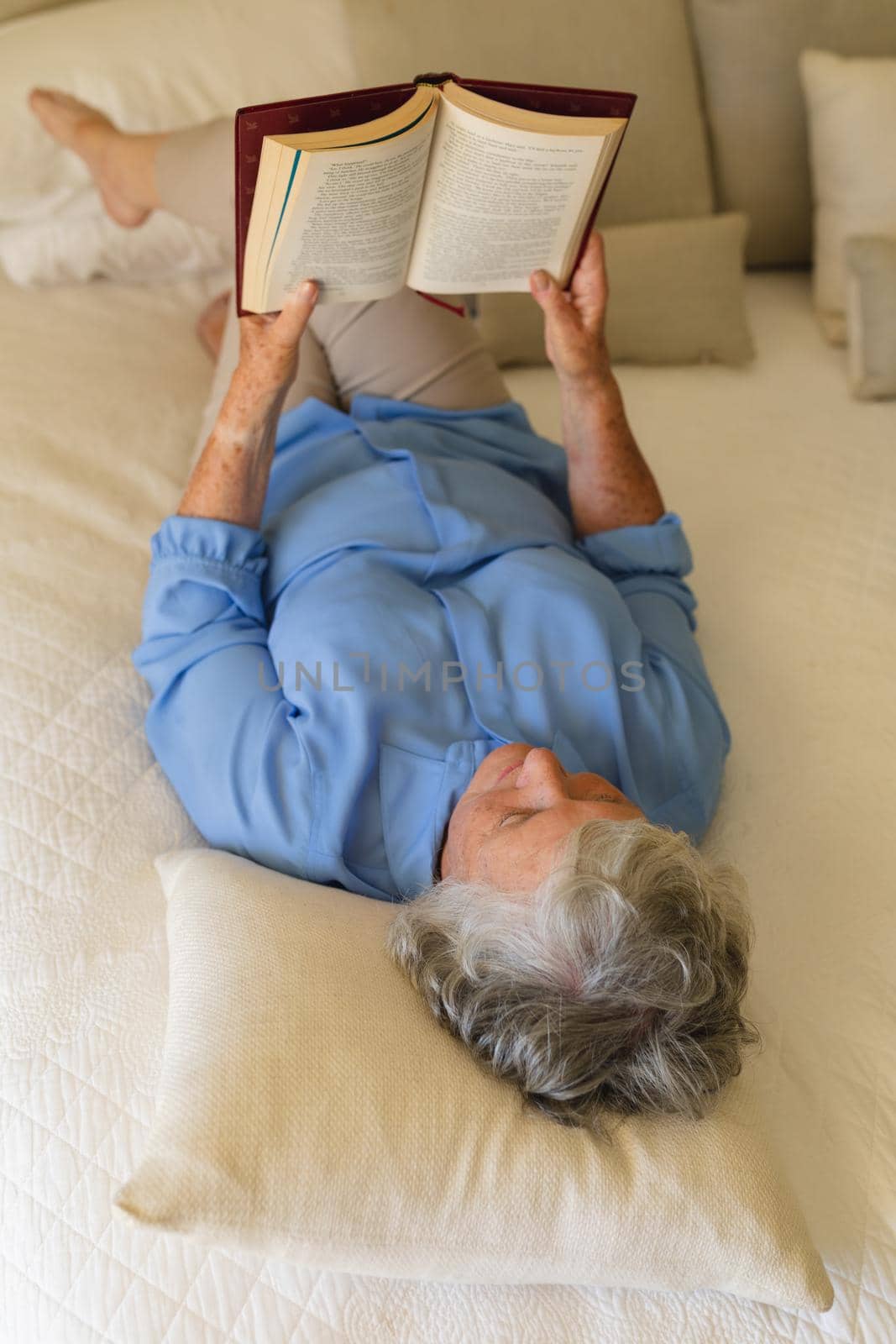 Senior caucasian woman lying in bed and reading book in bedroom. retreat, retirement and happy senior lifestyle concept.