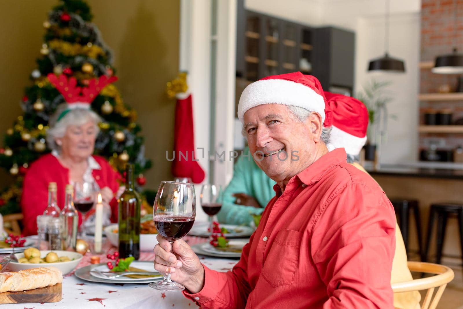 Happy caucasian senior man holding glass of vine at christmas table. christmas festivities, celebrating at home with friends.