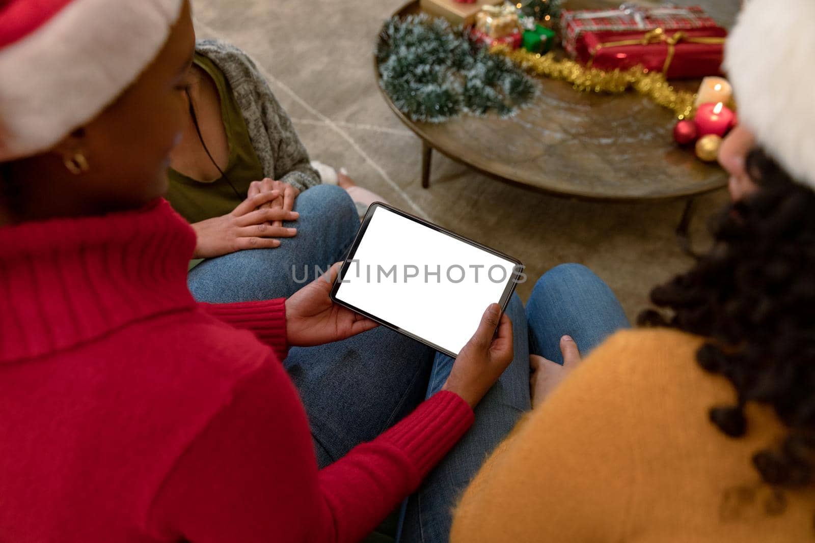 Group of happy diverse female and male friends using tablet with copy space at christmas time. christmas, festivity and communication technology.