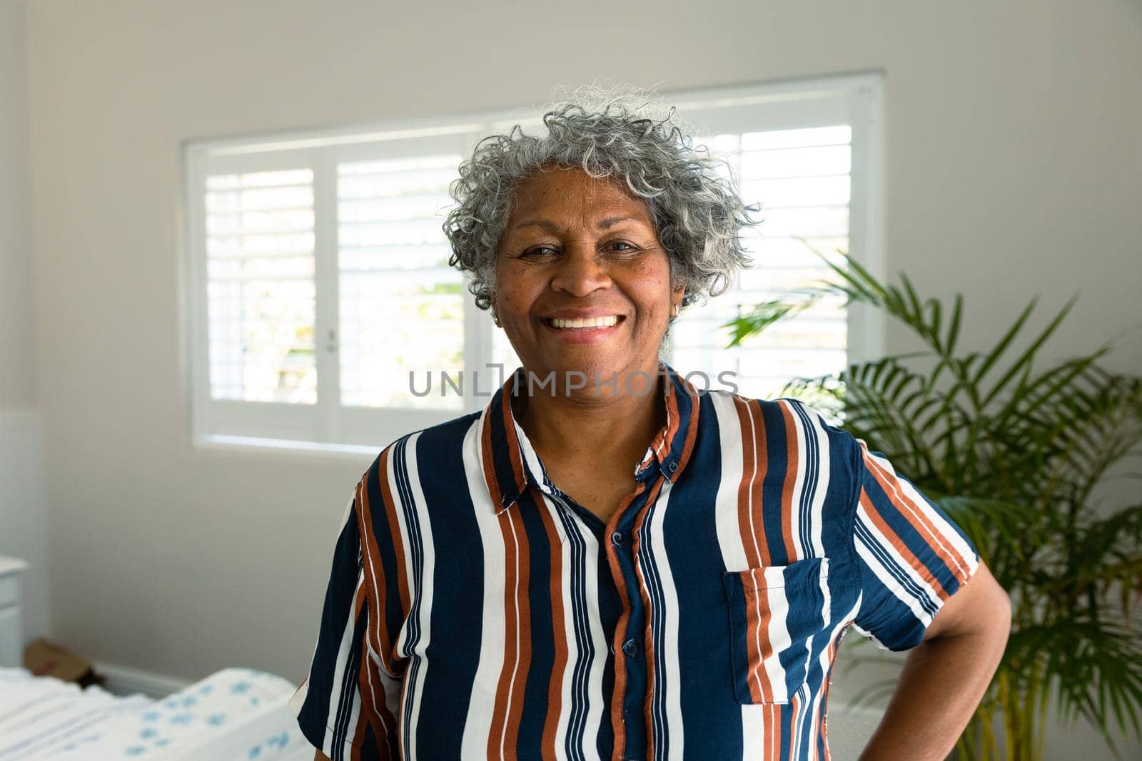 Happy african american senior woman standing in bedroom and looking at camera. healthy retirement lifestyle at home.