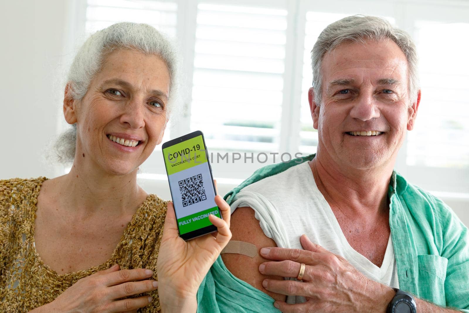 Smiling caucasian senior couple showing smartphone with covid 19 vaccine passport on screen. senior health and lifestyle during covid 19 pandemic.