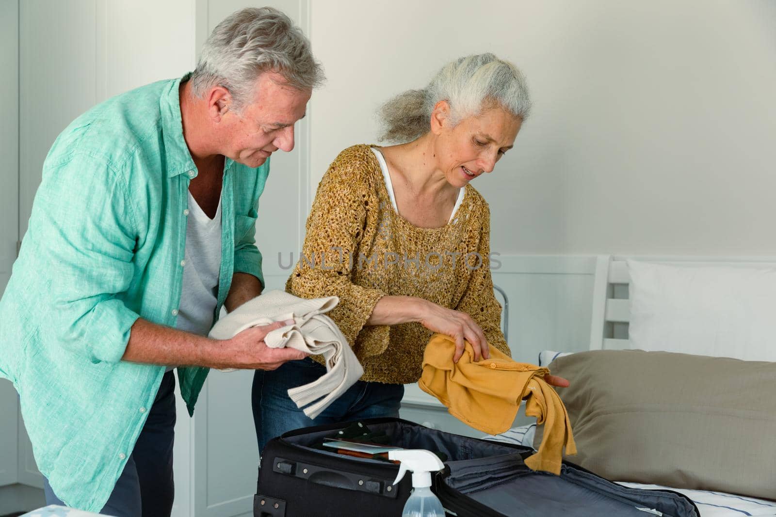Caucasian senior couple packing suitcase together and talking in bedroom. travel preparation during covid 19 pandemic.