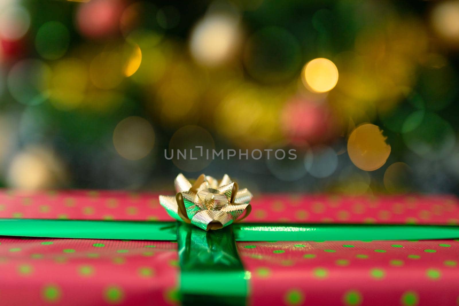 Christmas present in red paper with gold ribbon standing over christmas tree. christmas festivities, traditions and celebrating at home.