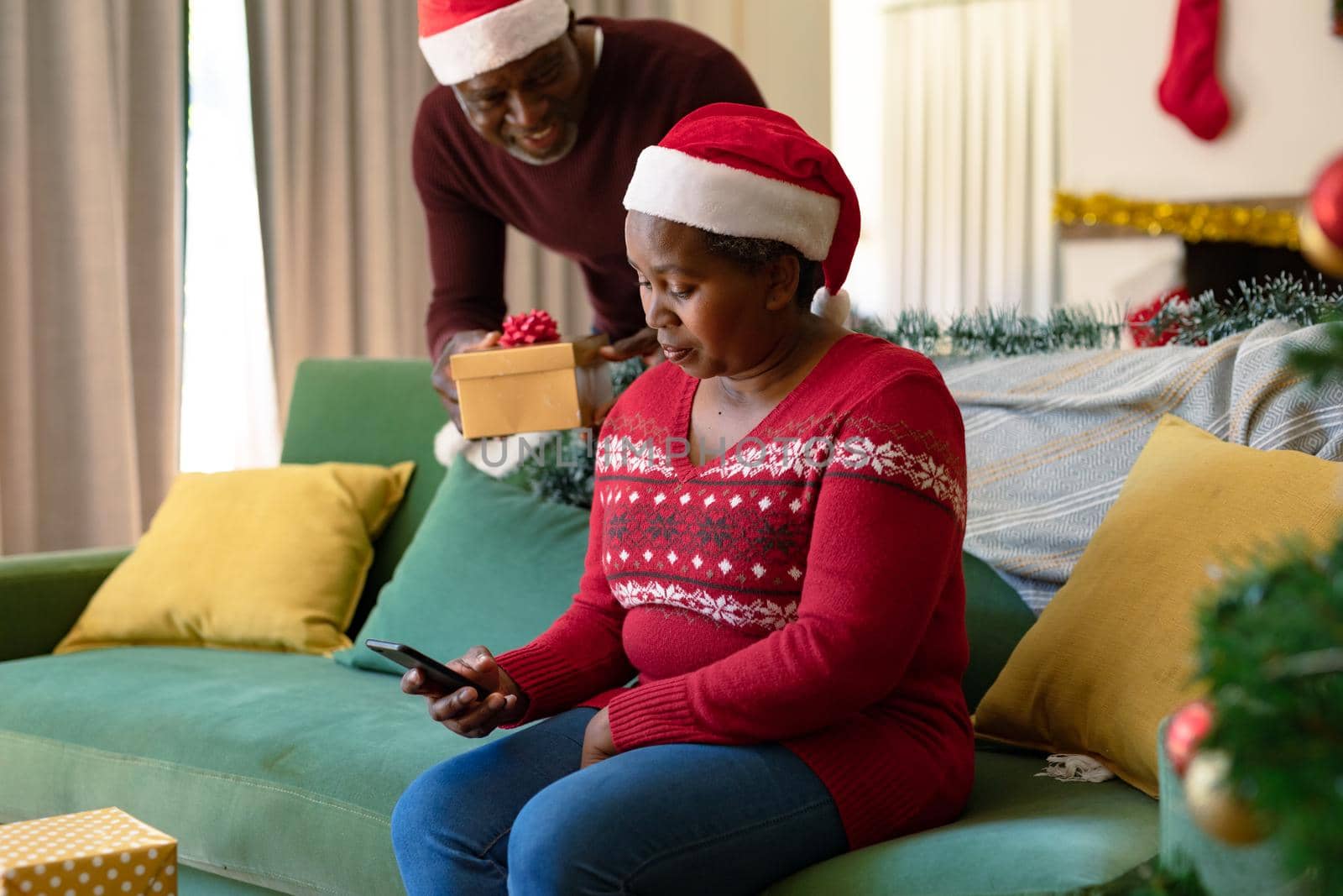 Happy african american senior couple in santa hats sharing presents at christmas time. retirement lifestyle and christmas festivities, celebrating at home.