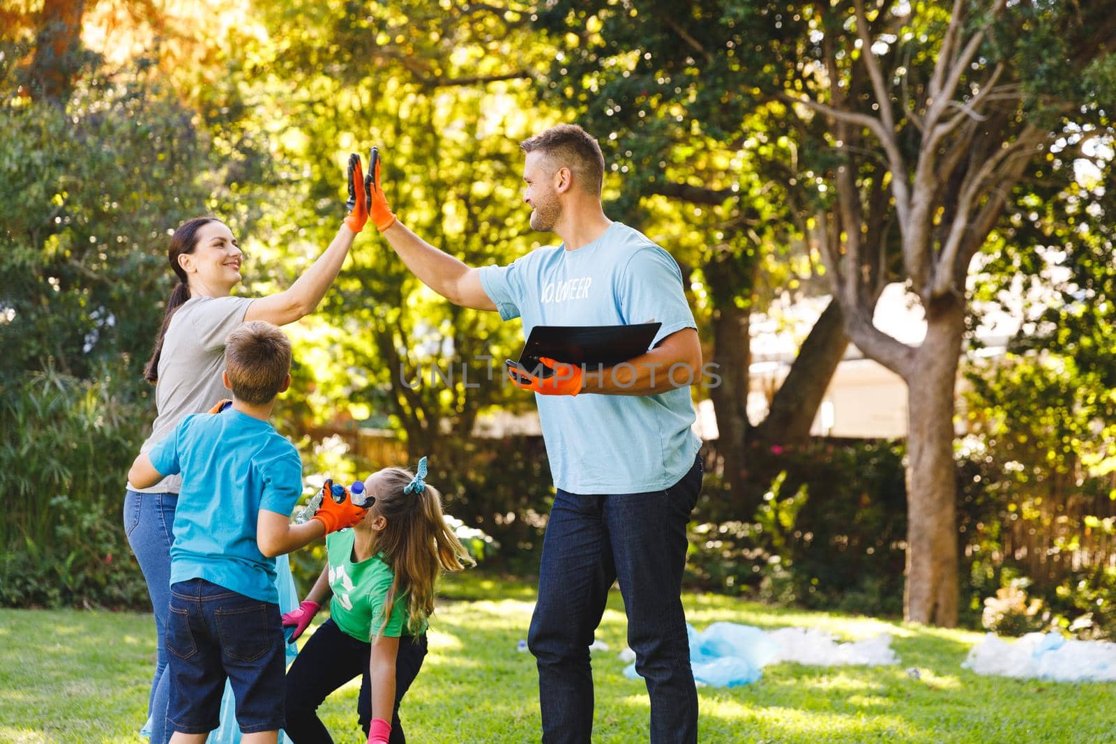 Caucasian parents, son and daughter high fiving, clearing up rubbish in the countryside by Wavebreakmedia