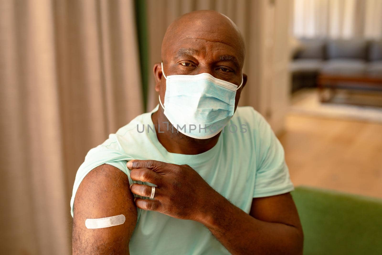 Portrait of african american senior man in face mask showing plaster after vaccination. senior health and lifestyle during covid 19 pandemic.